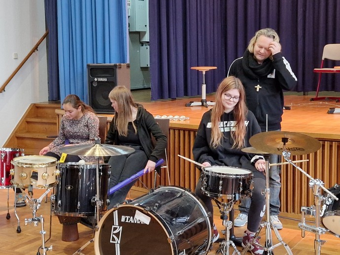 Schülerinnen und Schüler zusammen mit Dirk Brand am Drumset.