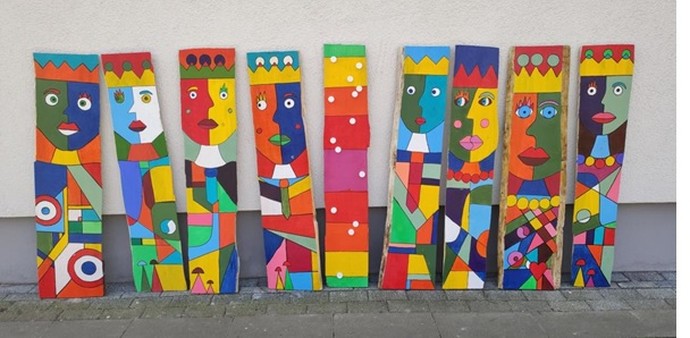 Ein Bild mit neun Woodpeople (Naturholzplatten, ca. 30 x 140 cm mit bunten Gesichtern und Figuren bemalt)